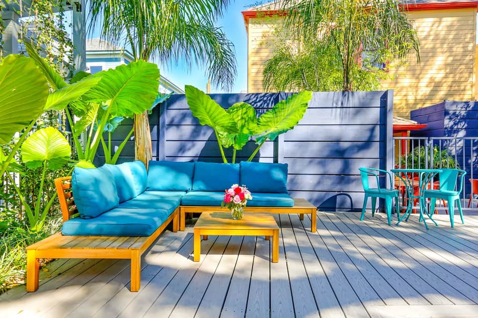 Colorful outdoor deck with blue sectional sofa, turquoise chairs, yellow coffee table, and tropical plants