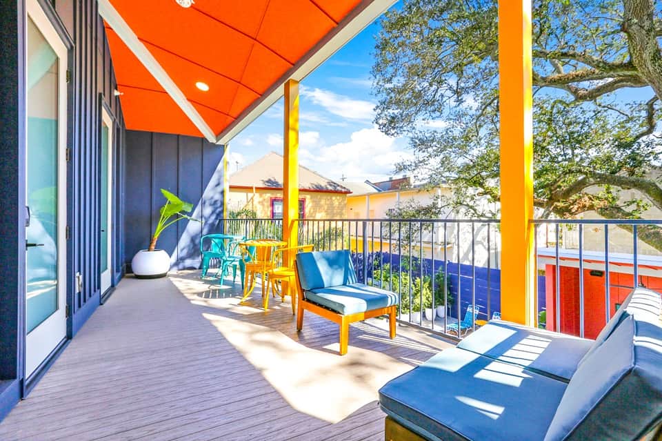 Colorful modern balcony with bright yellow and orange posts, red umbrella, and blue lounge chairs