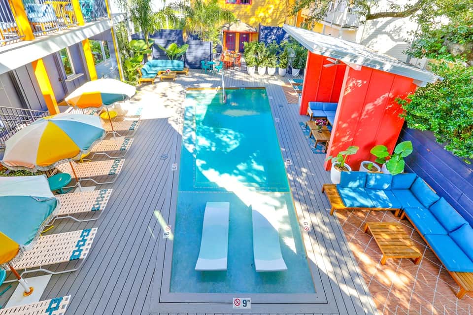 Colorful urban pool courtyard with bright umbrellas, lounge chairs, and surrounding multi-story apartment buildings
