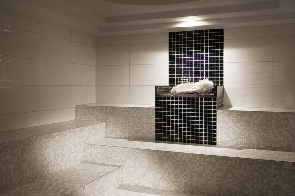 Luxurious spa room with multi-level white tiled benches and black tile accent wall
