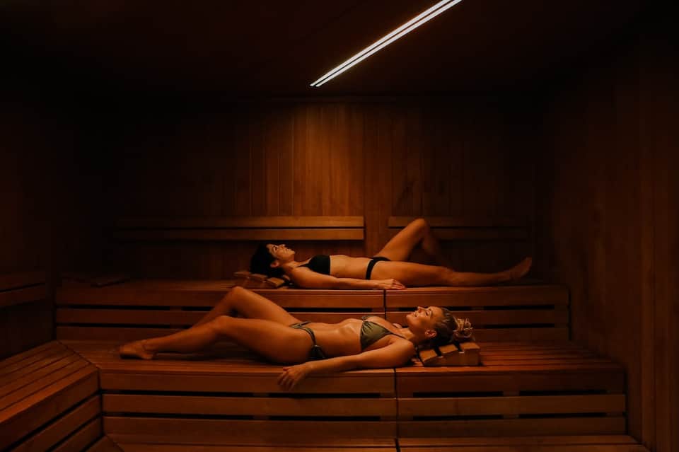 Spa sauna interior with two people relaxing on wooden benches under warm overhead lighting