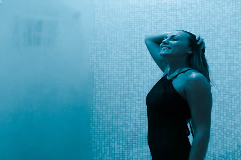 Woman swimming underwater in pool with blue mosaic tile walls and natural light