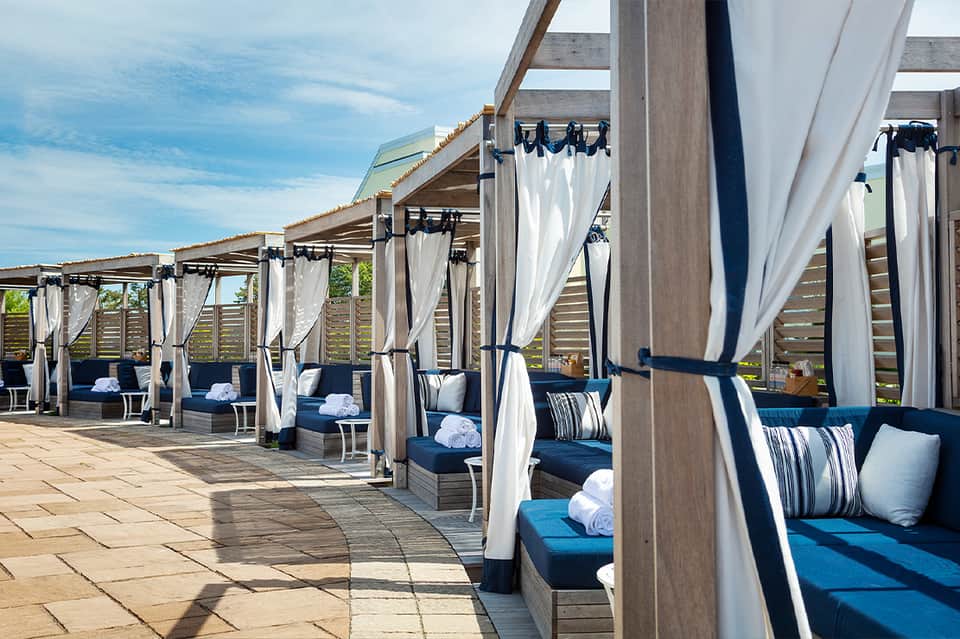 Luxury beachfront cabanas with white curtains, blue cushions, and ocean views
