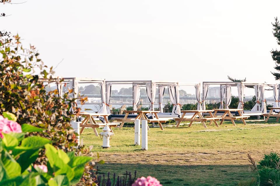 Beachfront event setup with white cabanas and wooden furniture overlooking water