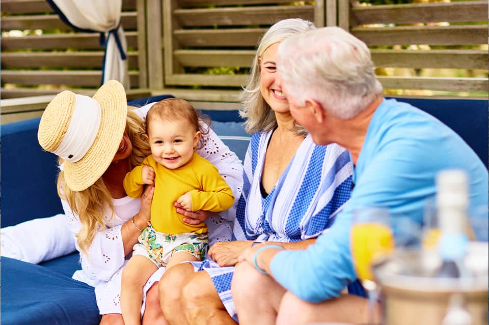 Three generations of family relaxing on blue lounge chair poolside on a sunny day wearing summer attire