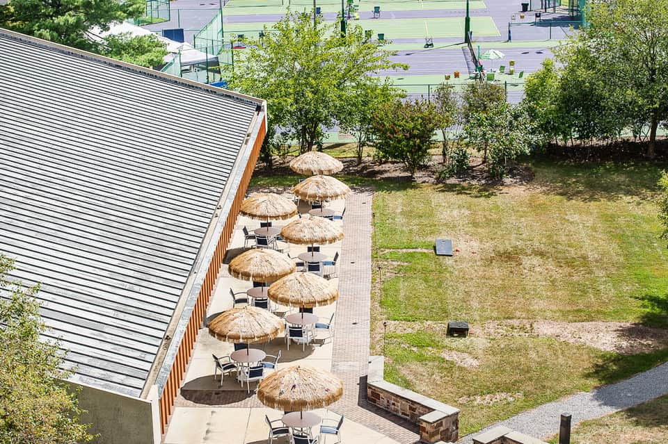 Outdoor patio with thatched umbrellas and lounge chairs beside a modern building with metal roof