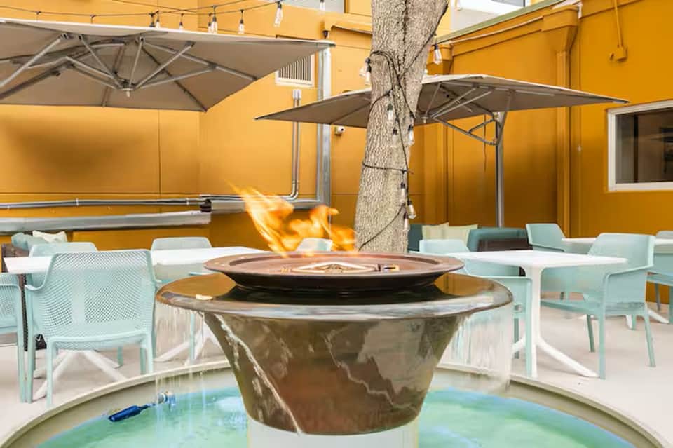Resort patio with fire pit, yellow walls, umbrellas, light blue chairs, and palm tree