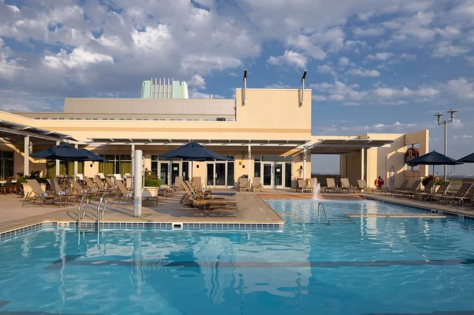Resort swimming pool with covered outdoor area, lounge chairs, and blue umbrellas