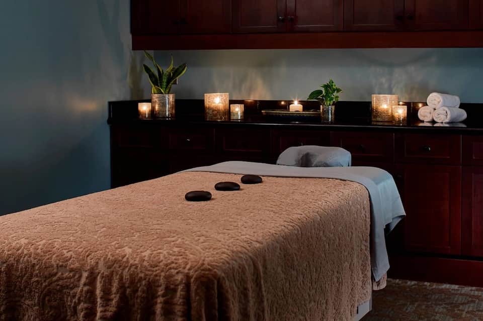 Spa massage room with hot stones, white linens, dark wood cabinetry, and candlelit ambiance