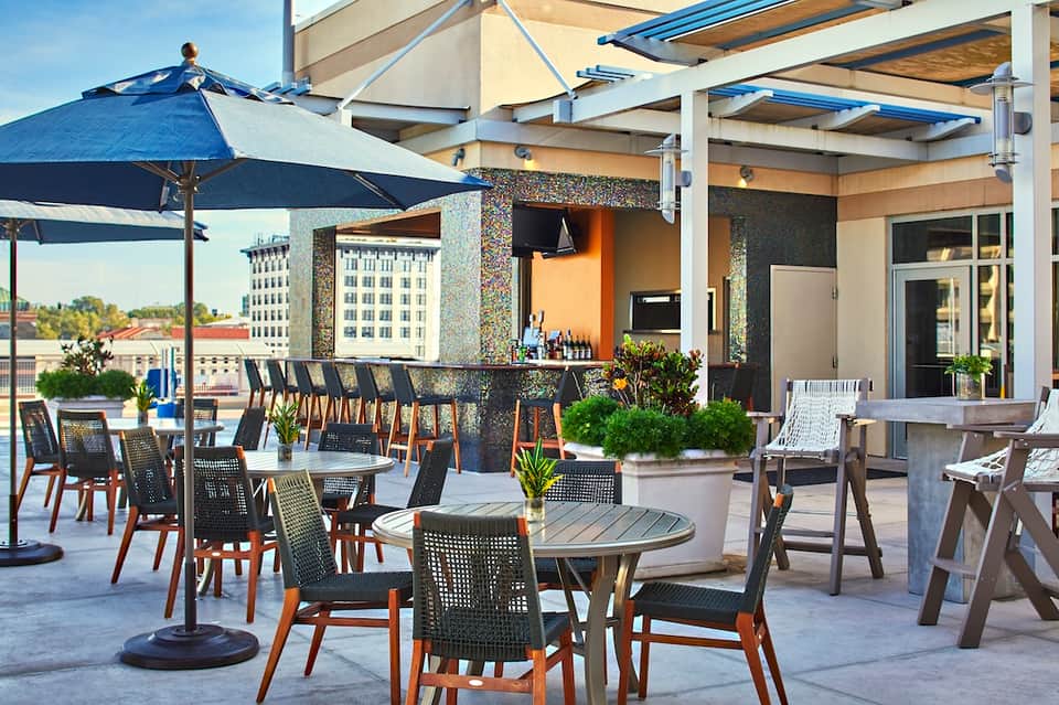 Rooftop bar and lounge with blue umbrellas, modern seating, and city skyline views
