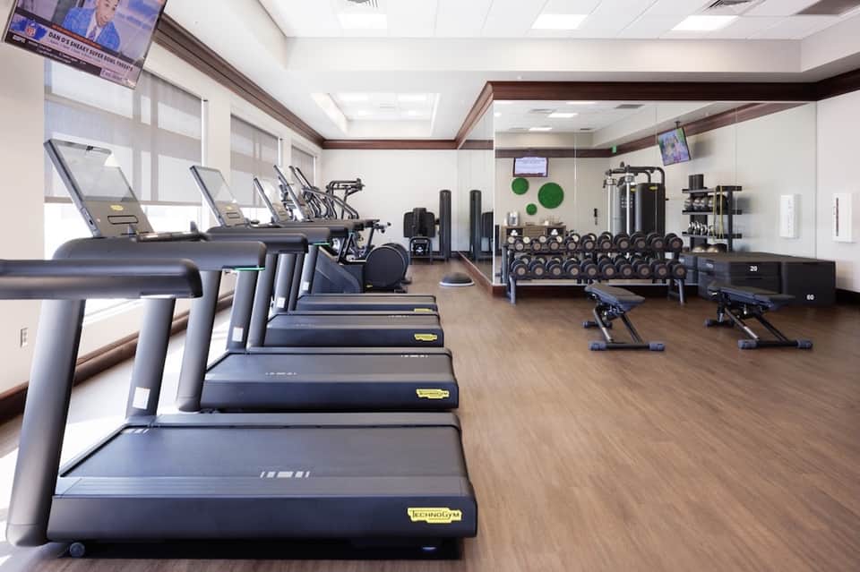 Modern hotel fitness center with rows of treadmills, free weights, and exercise equipment