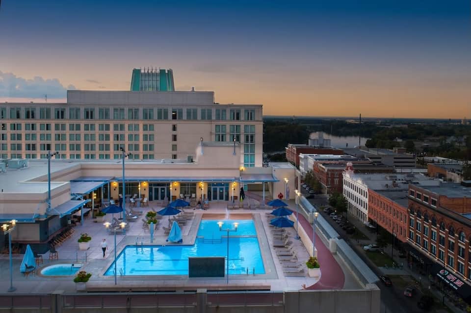 Rooftop pool at dusk with blue umbrellas, hotel buildings, and cityscape view at golden hour