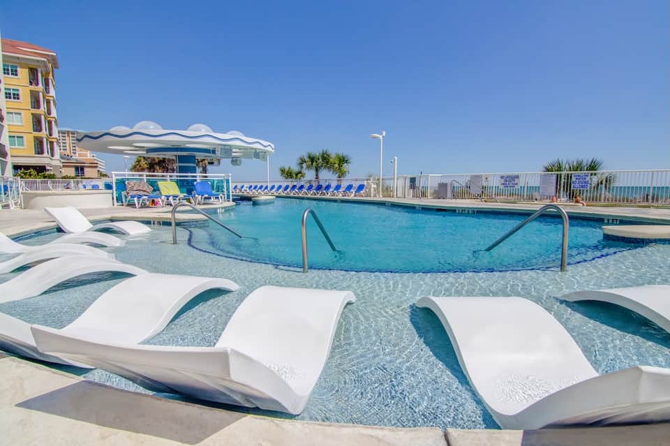Oceanfront resort pool with lounge chairs, palm trees, and beachside cabana structure