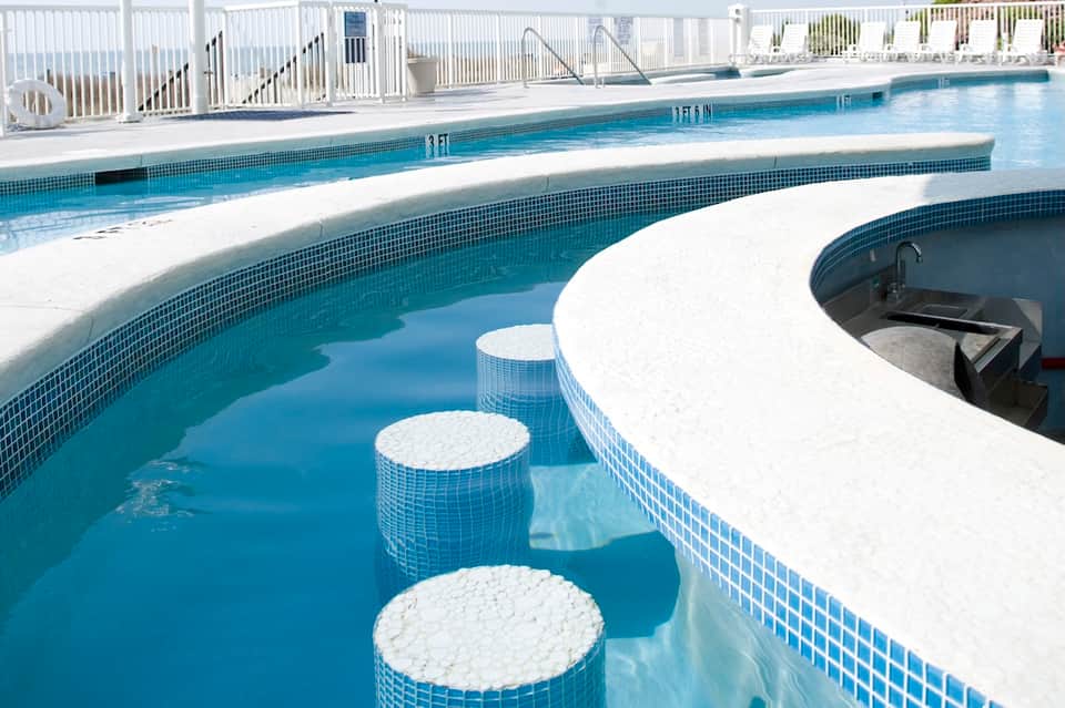 Modern lap pool with spa tub, white safety railings, lounge chairs, and coastal views