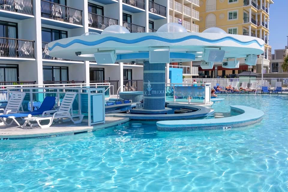 Resort pool area with wave-shaped canopy pavilion, lounge chairs, and clear turquoise water
