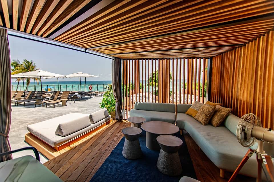 Beachfront lounge area with modern seating, wooden slat screens, and turquoise ocean view beyond