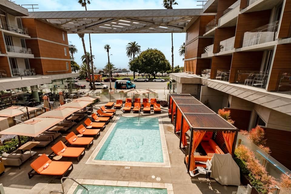 Resort courtyard pool with orange loungers, cabanas, and surrounding modern buildings