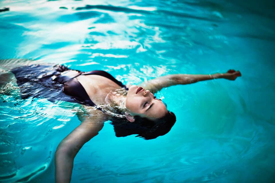 Person floating on back in bright turquoise swimming pool water