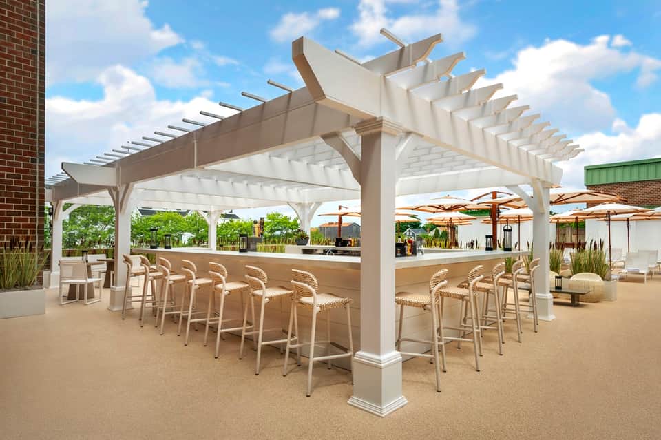 Outdoor bar area with white pergola, bar seating, and umbrellas