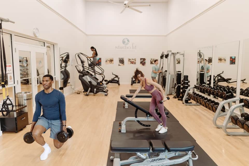 Bright fitness center with exercise equipment, mirrors, and people working out