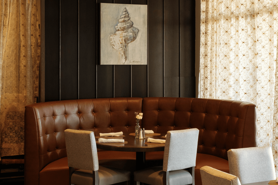 Intimate lounge seating with brown leather banquette, seashell artwork, and patterned wallpaper