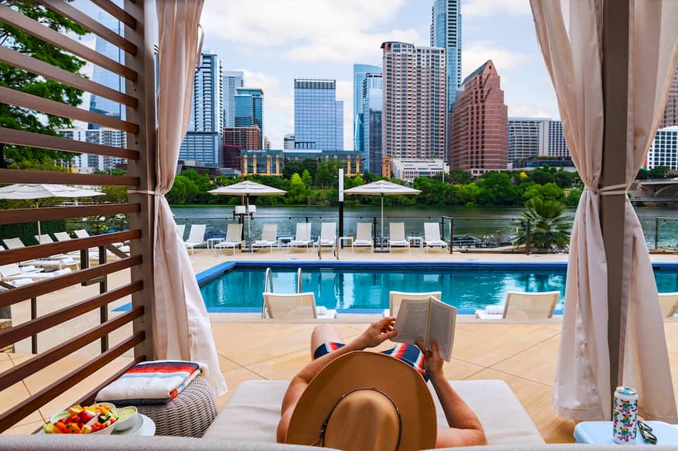 Urban resort pool lounge with city skyline views, private cabana, and waterfront backdrop