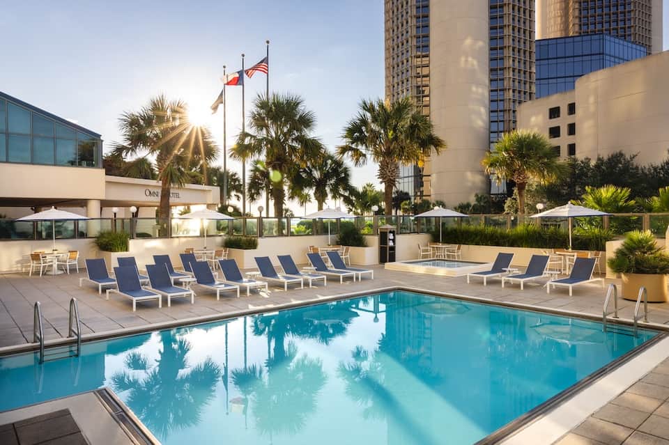 Urban resort pool with lounge chairs, umbrellas, palm trees, and tall buildings