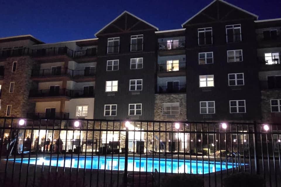 Apartment building exterior at night with lit windows and illuminated courtyard pool