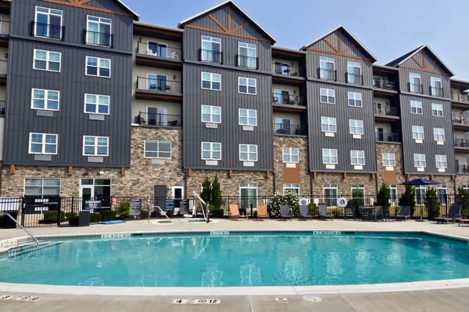 Multi-story apartment building with dark metal siding, stone base, and outdoor pool in foreground