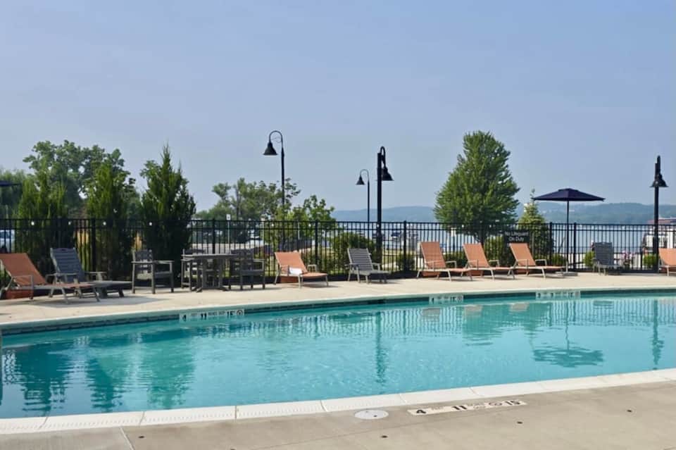 Lakeside pool deck with lounge chairs, umbrellas, black railings, and mountain backdrop