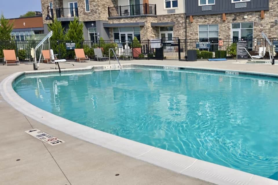 Resort pool with clear turquoise water, lounge chairs, multi-story stone and metal residential building