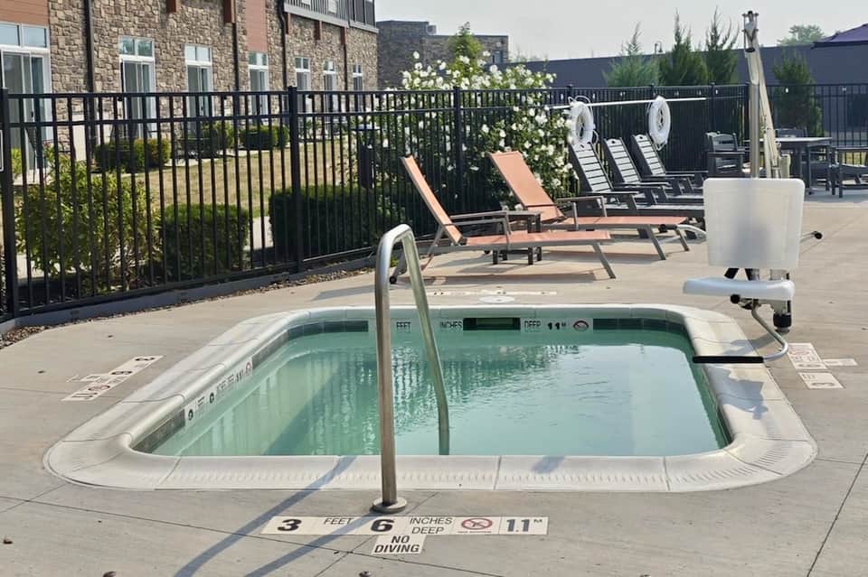 Small rectangular hot tub on patio with lounge chairs and flowering vines against stone and brick building