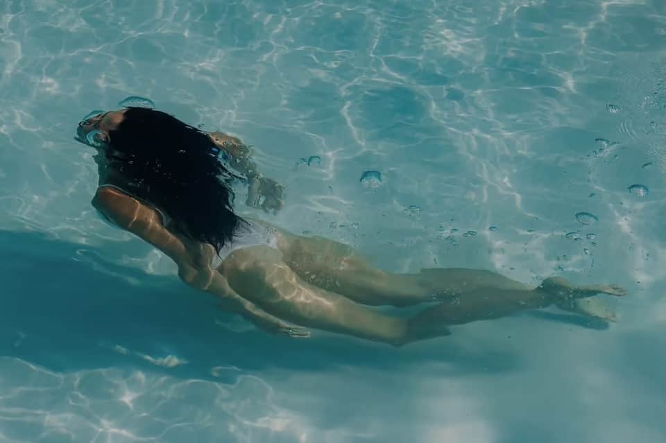 Person snorkeling in clear turquoise shallow water with visible fish and sun reflections