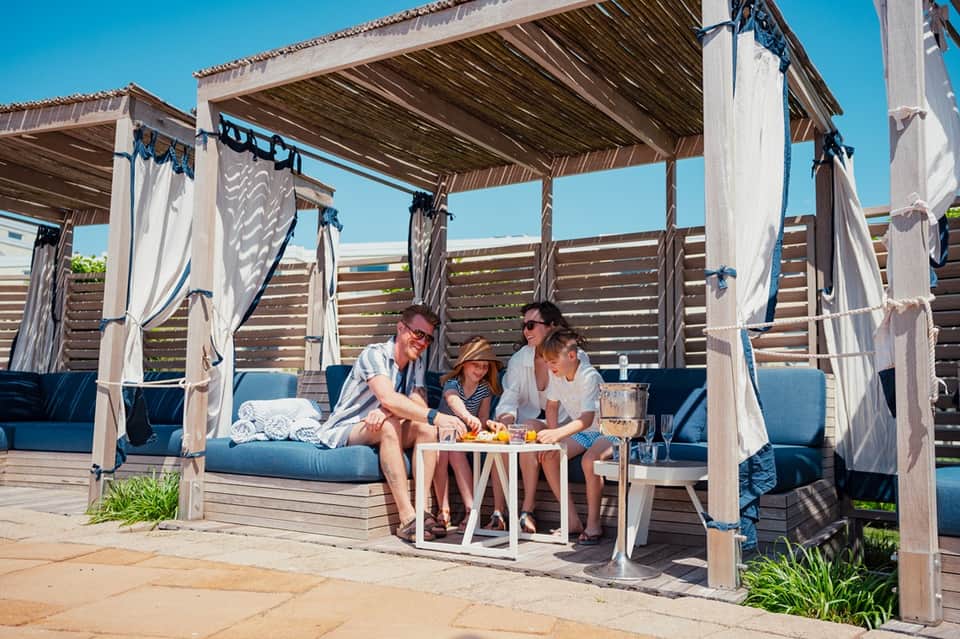 Outdoor cabana lounge with blue cushioned seating and white curtain drapes