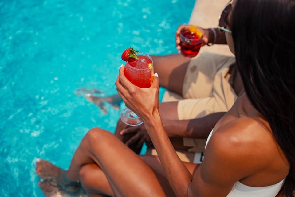 Woman enjoying cocktails poolside in tropical setting with crystal clear turquoise water