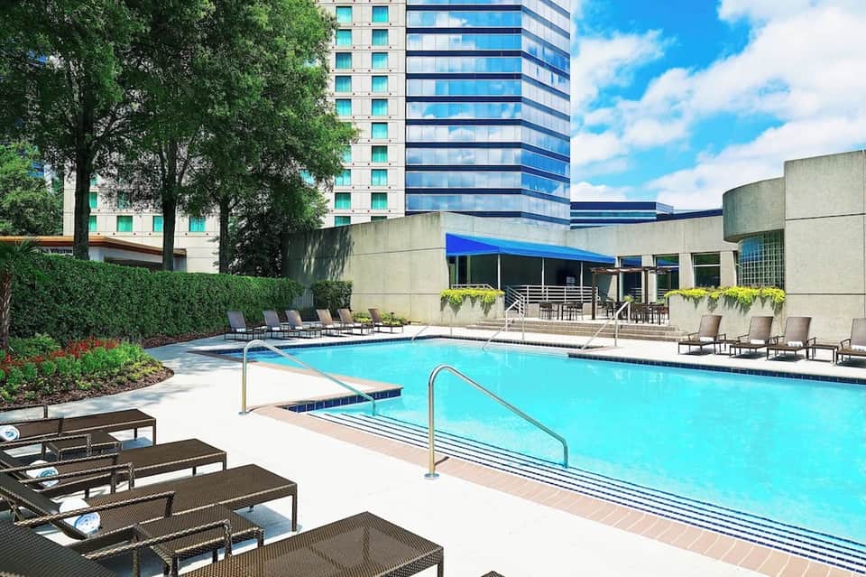 Hotel outdoor pool with turquoise water, lounge chairs, modern building facade, and landscaping