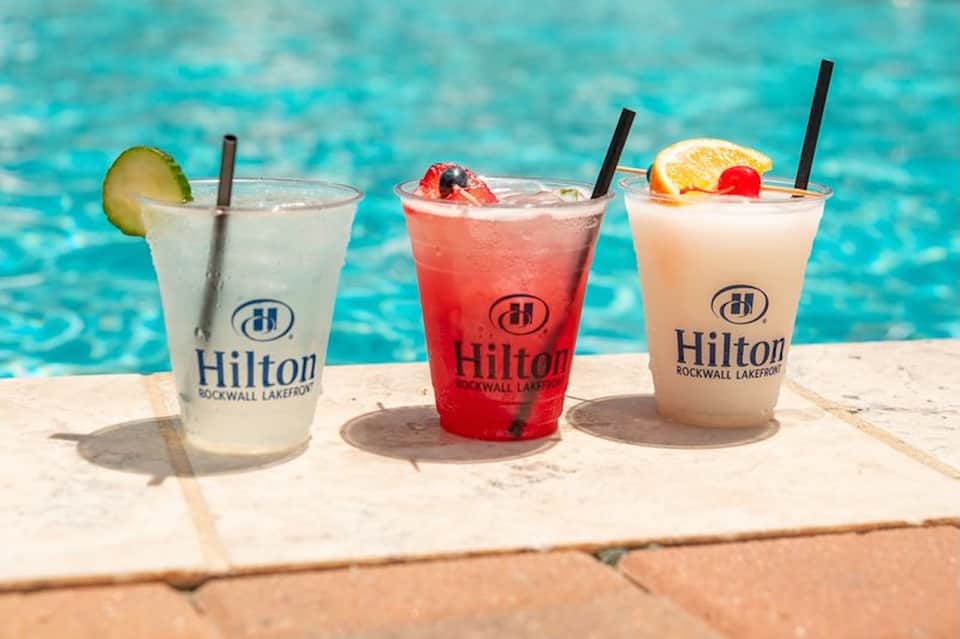 Three colorful cocktails with Hilton branding at poolside on sunny day