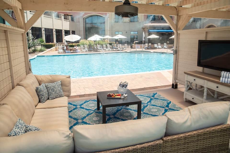Covered lounge area overlooking large resort pool with umbrellas, comfortable seating, and patio furniture