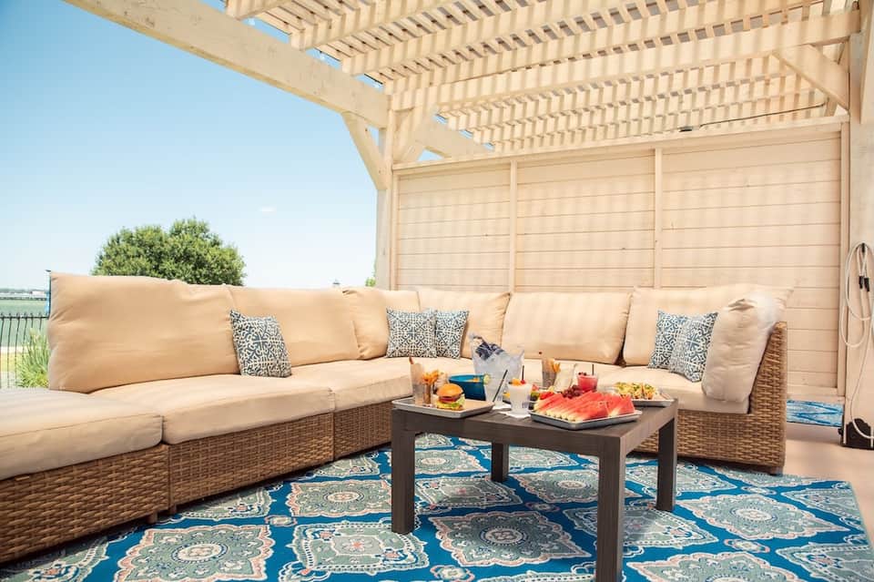 Upscale outdoor patio with wicker sectional sofa, pergola shade structure, and patterned rug