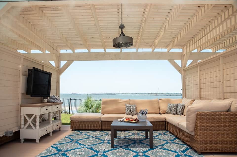 Covered waterfront patio with wicker furniture, fireplace, and bay views