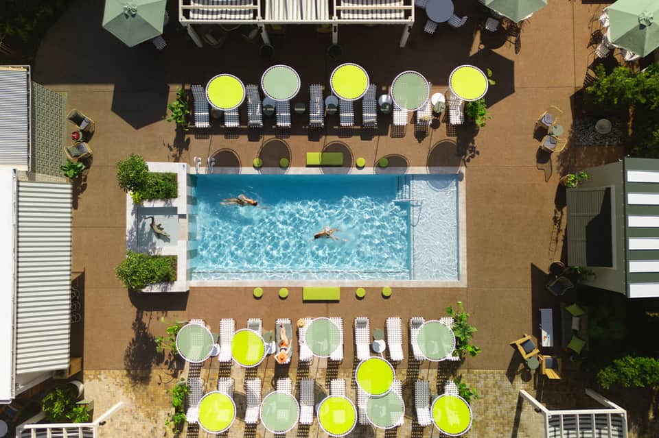 Overhead view of hotel pool with cabanas, yellow umbrellas, and lounge seating on sandy deck