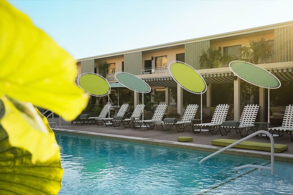 Resort swimming pool with green and white umbrellas, lounge chairs, and modern building facade