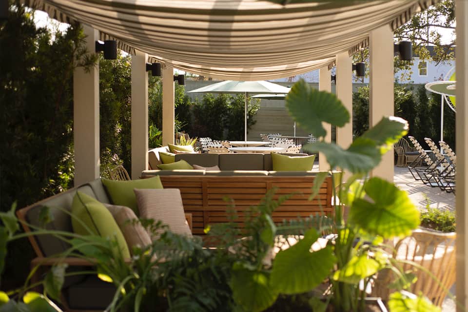 Shaded outdoor lounge area with striped awning, wooden seating, and views through palm trees and greenery