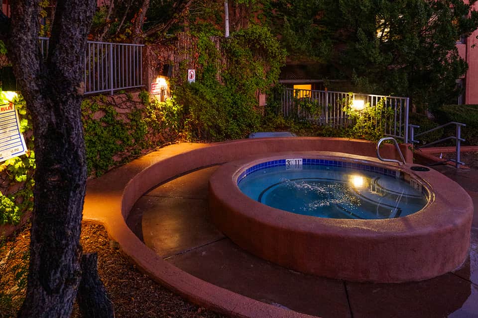 Illuminated hot tub surrounded by desert landscaping and ivy-covered walls at night