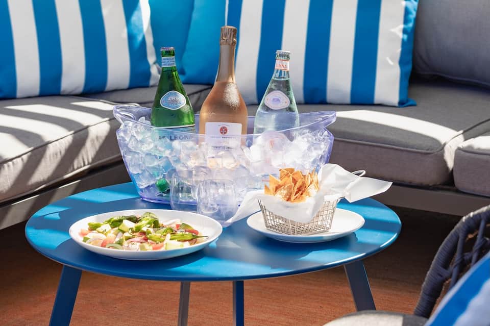 Poolside table with champagne bucket, appetizers, salad, and blue striped lounge chairs in background