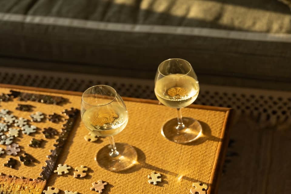 Two wine glasses on yellow table napkin with puzzle pieces and outdoor structure in background