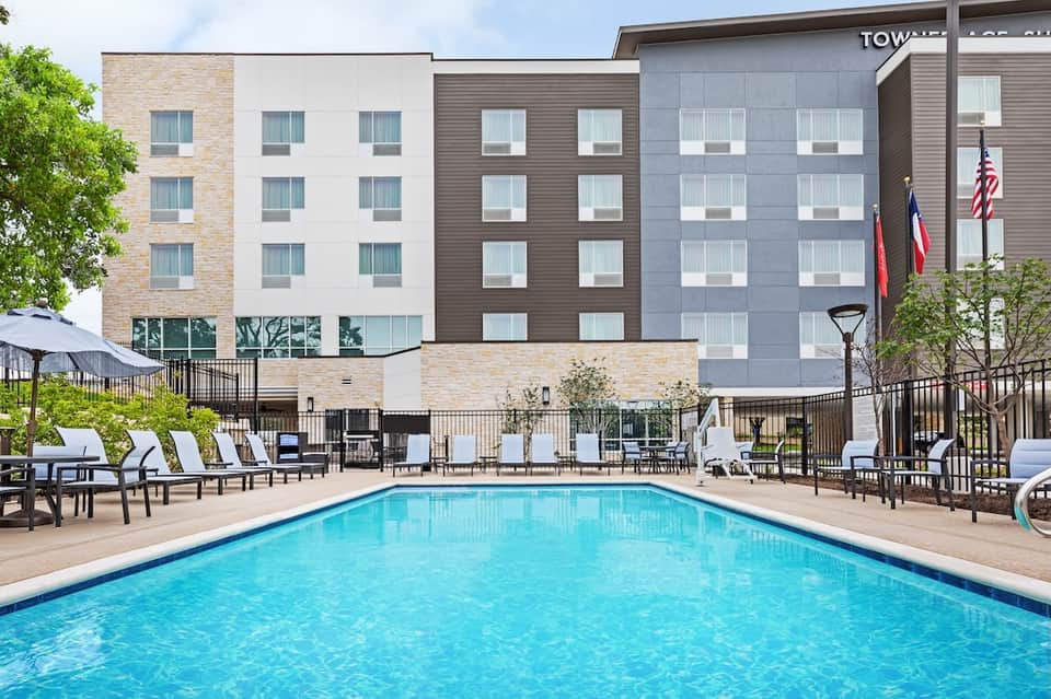 Modern hotel exterior with multi-story building, outdoor swimming pool, lounge chairs, and landscaping
