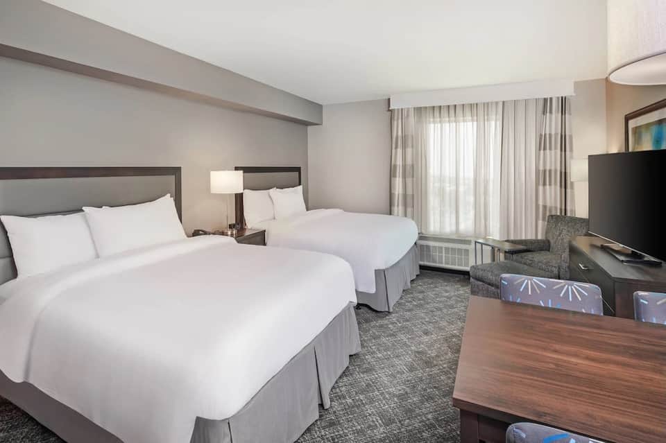 Hotel room with two queen beds, neutral décor, TV, and seating area