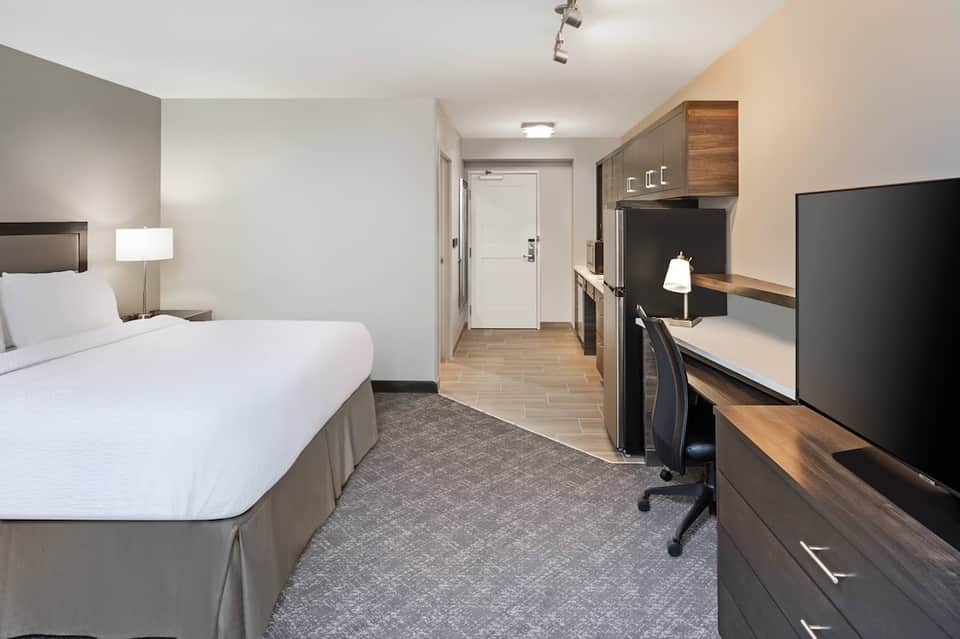 Modern hotel guest room with queen bed, work desk, dark wood cabinetry, and neutral décor