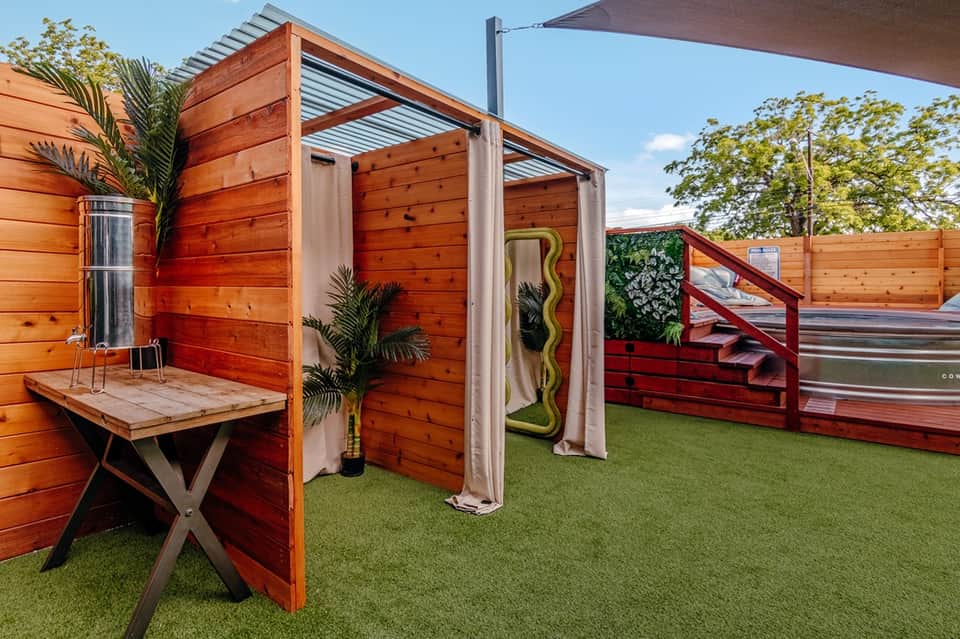 Rooftop recreational area with wooden structures, shade covers, artificial grass, and planter pots